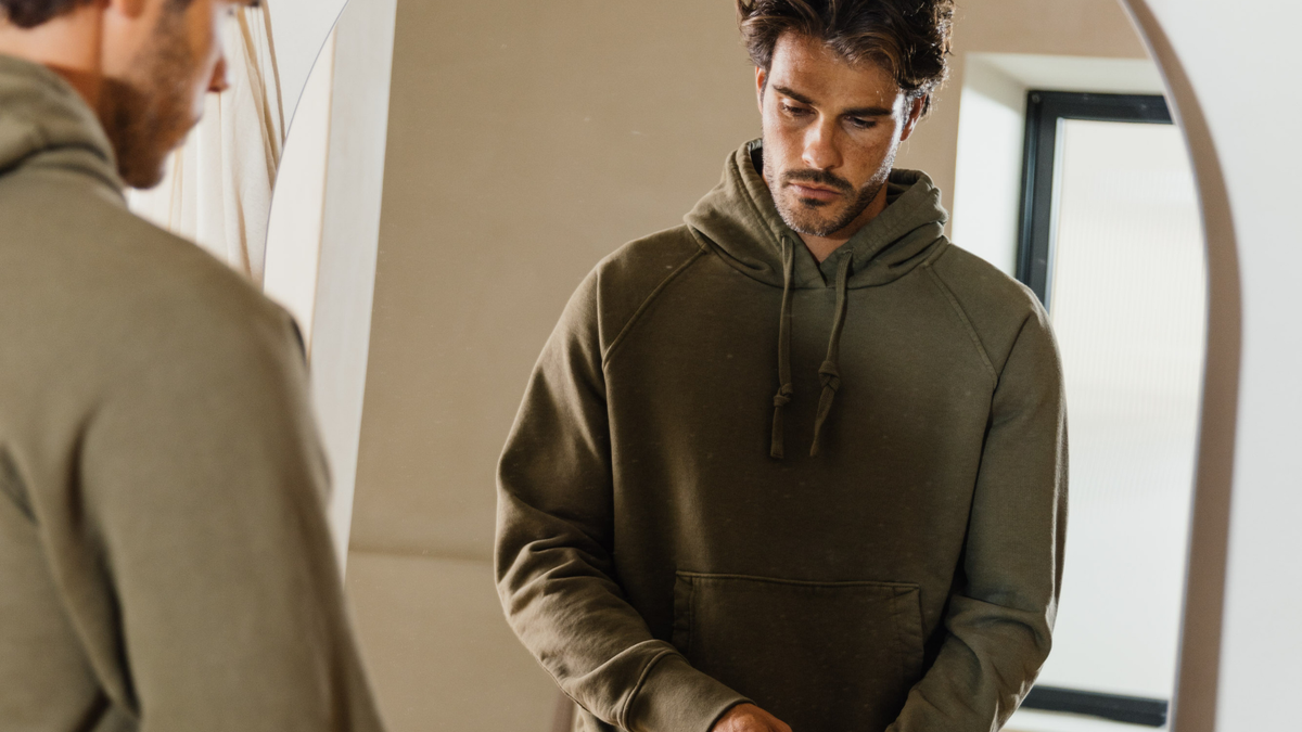A man in an olive Apollo X hoodie, looking down in a quiet room